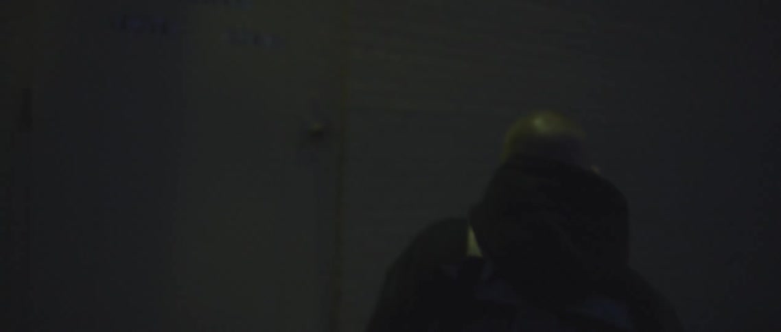 A bald man in a hooded coat walks down an alley at sunset and enters a door that refers to freedom fighters youth boxing
