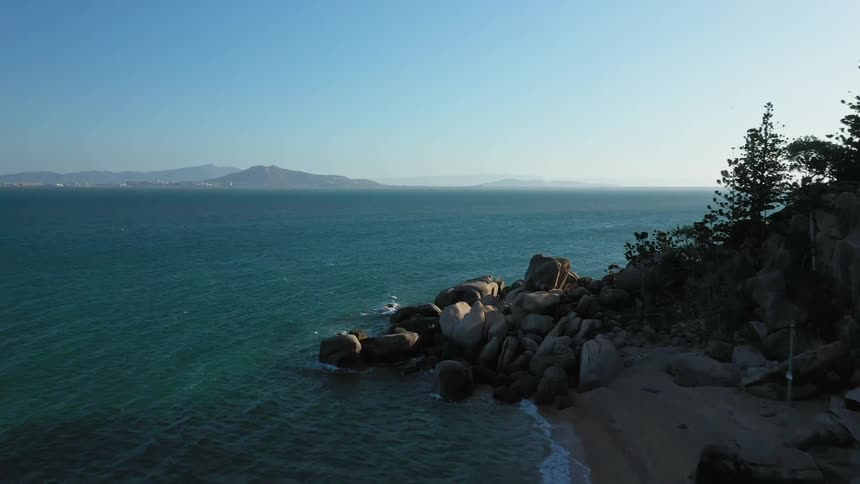 Ocean waves splash against a rocky shore and a sandy beach on a sunny day