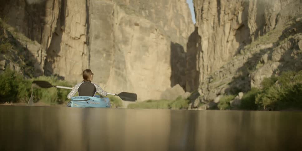 A woman kayaks on a lake bordered by steep walled mountains