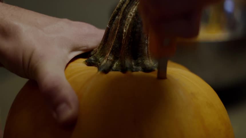 A man pushes a serrated knife into the top of a pumpkin
