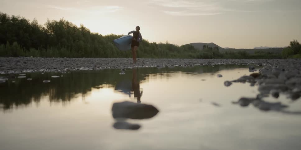 Woman carrying kayak alongside a river bank