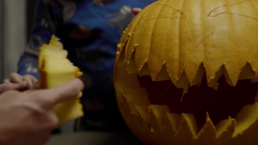 An adult and child are pulling out a piece pumpkin that has been carved out to make a jack olantern