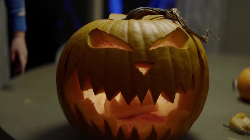 A man turns a carved pumpkin around to show a glowing jagged smile