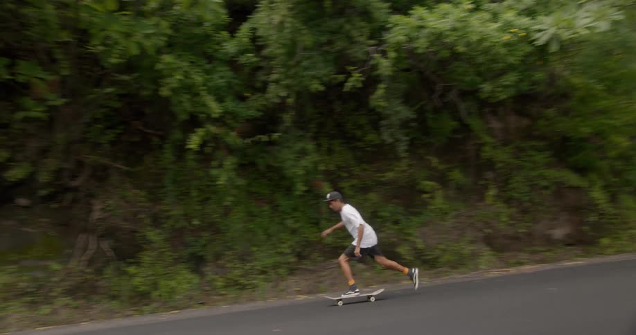 A boy skateboarding down a road on a slope