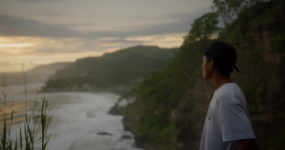 A young man stands on a coast and gazes out over the ocean