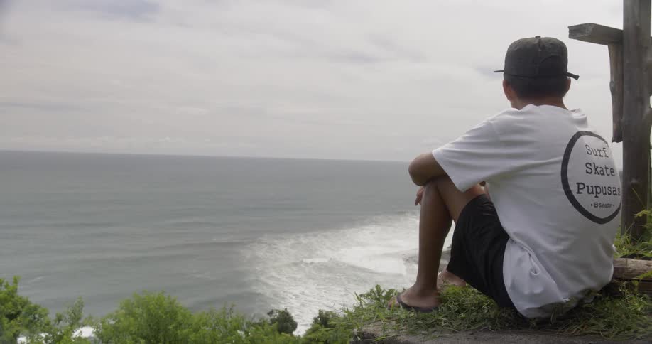 A man sits on the edge of a cliff over the ocean