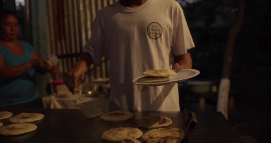 A man removing tortillas from a commercial cook top with a spatula and placing them on a white plate