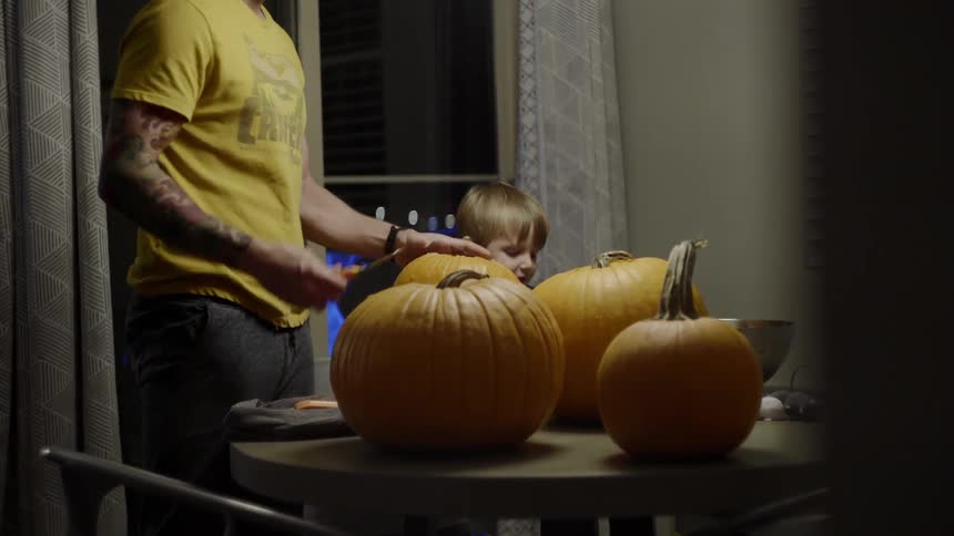 A man and a boy carving pumpkins indoors at night