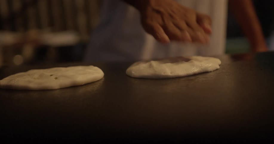 A person prepares flat bread on a large griddle
