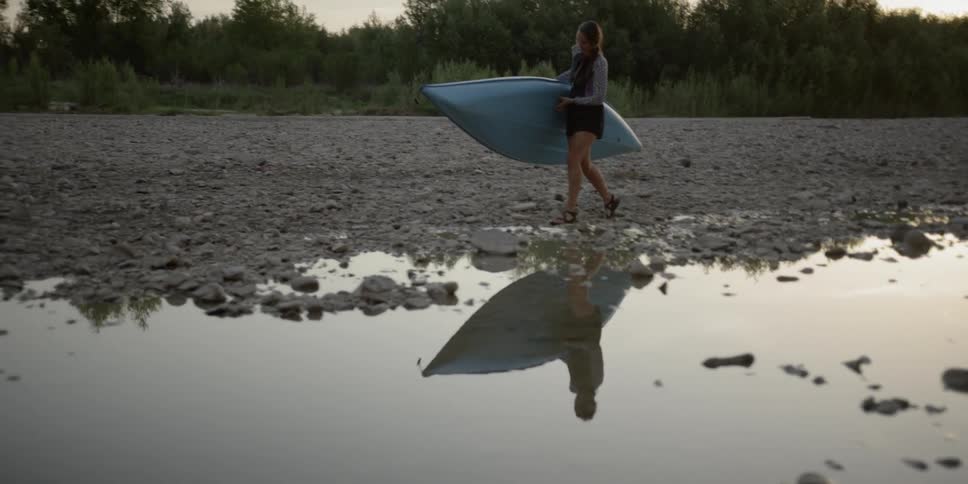 A young woman carrying a kayak along a rocky shore