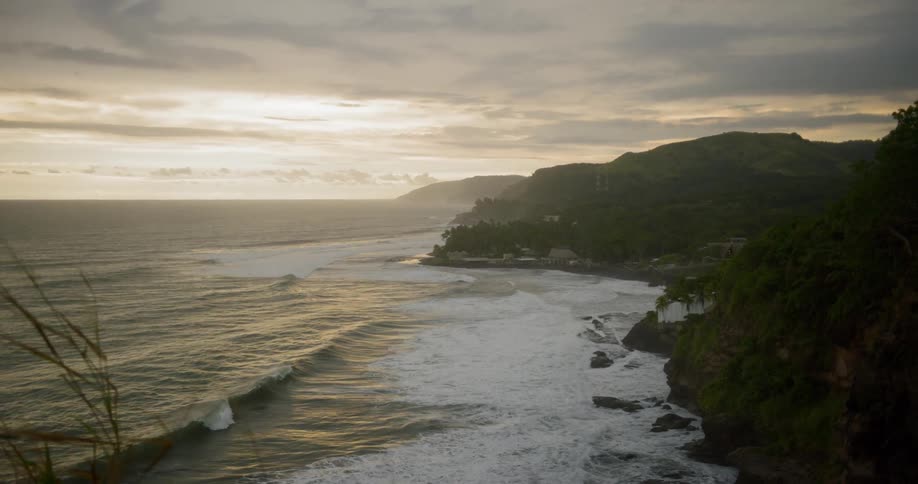 A view of waves calmly crashing into a beach with rocky cliffs at sundown