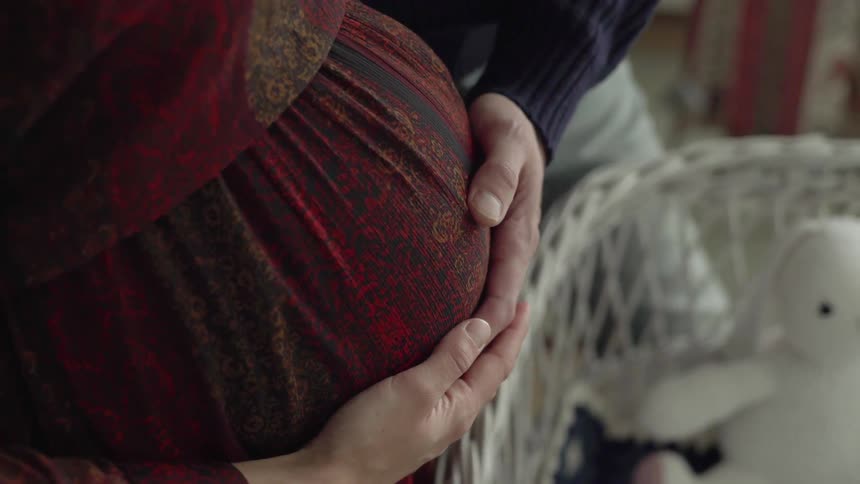 A man places his hand on the stomach of his pregnant partner and gently feels the movement of an unborn child