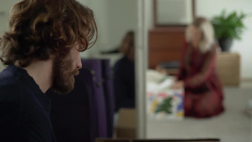 A man and a very pregnant woman are sitting on the ground in joining rooms going through moving boxes