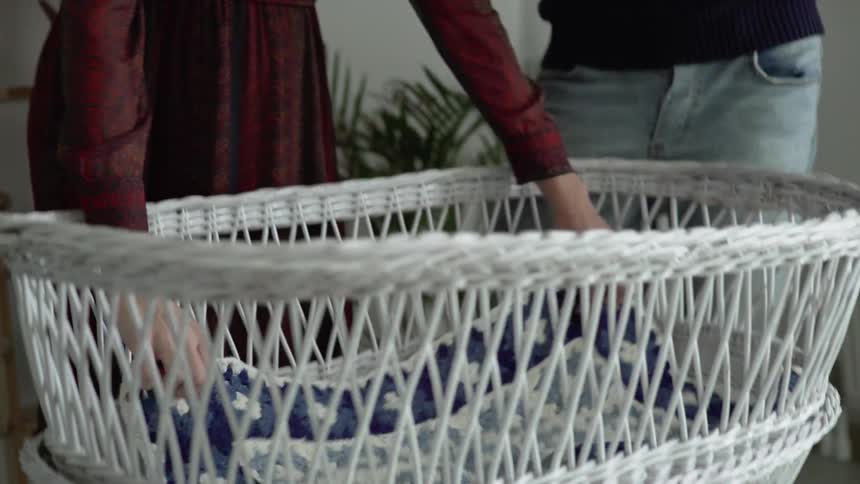 A woman unfolds a blanket and places it in a bassinet