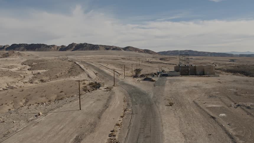 A dirt road in an arid location alongside telephone lines and an infrastructure installation