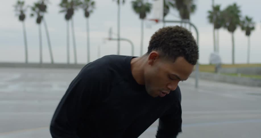 A man dribbles a basketball between his legs on an outdoor basketball court