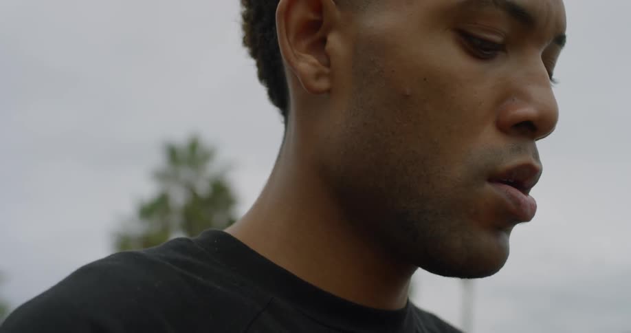 A black man standing outdoors looking around and thinking