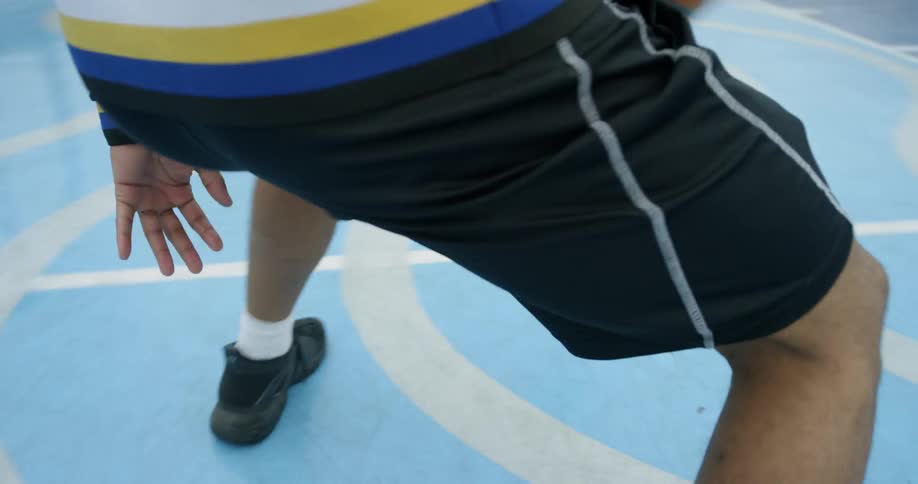 A male dribbles a ball back and forth under his leg on an outdoor basketball court