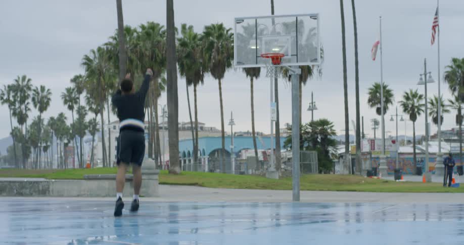 Man bounces a basketball on an outdoor court then tosses the ball at a hoop