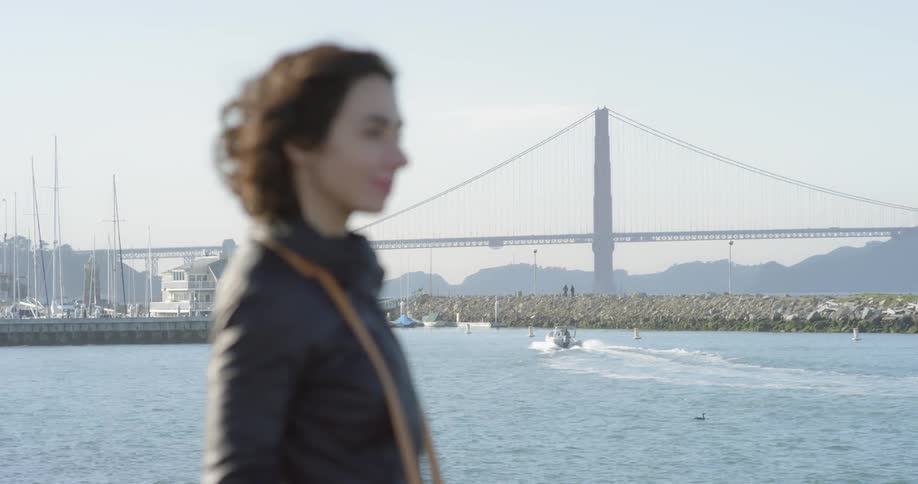 A woman is smiling by the shore as a boat passes by