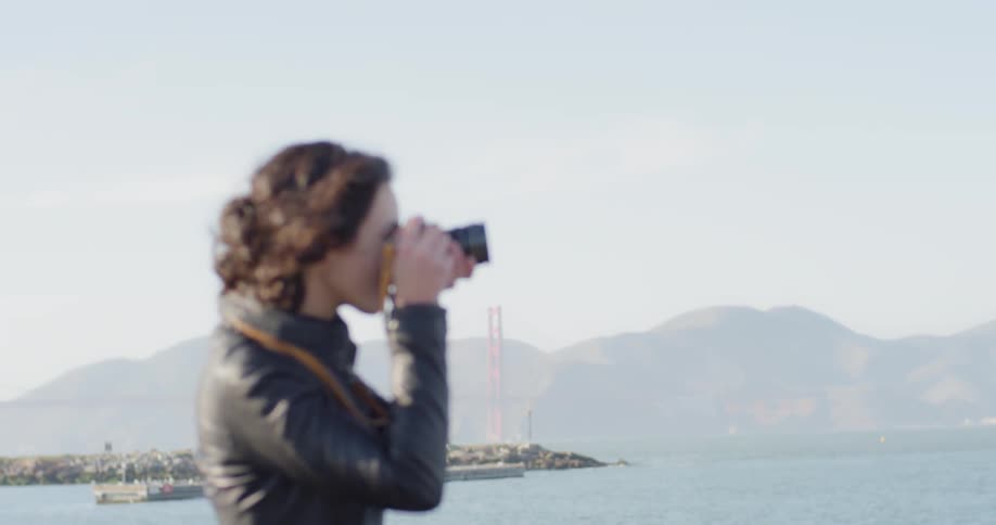 Woman stands near ocean taking photographs
