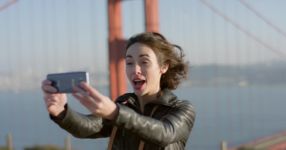 A woman is taking a selfie by a bridge