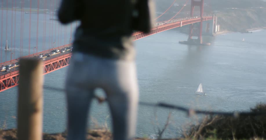 A woman is standing by a railing near a large bridge