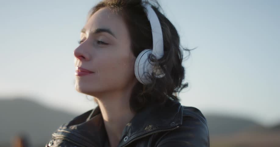 A young white woman listens to headphones while outdoors