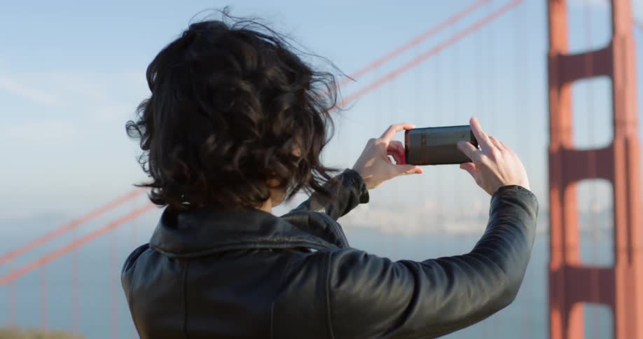 Woman holds phone out in front of her to take a photo of the golden gate bridge