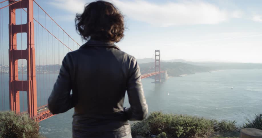 Woman in a leather jacket looks down at the golden gate bridge