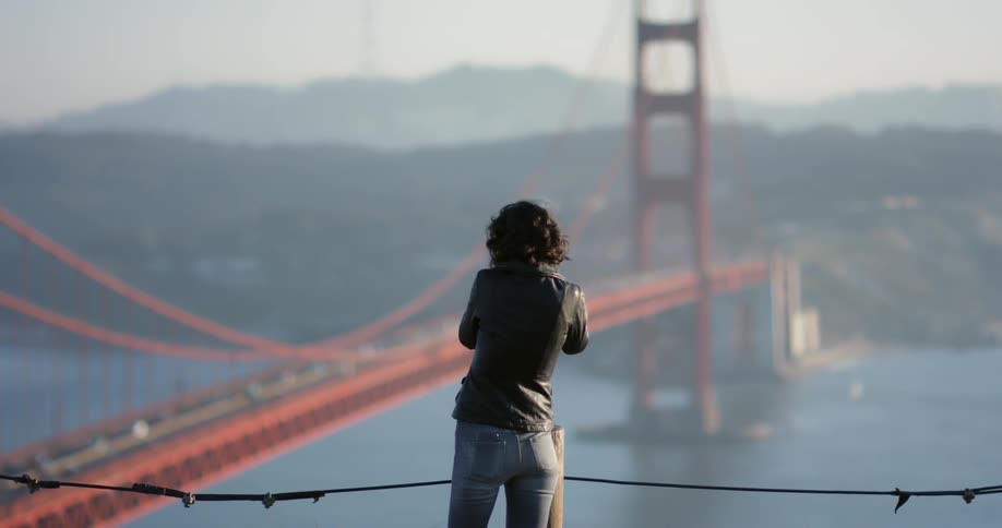 A woman walks over to the railing to take photographs of a bridge