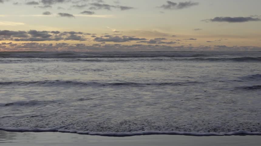 Waves Rolling In at Sunset on Beach Shoreline with Golden Sky Reflections.