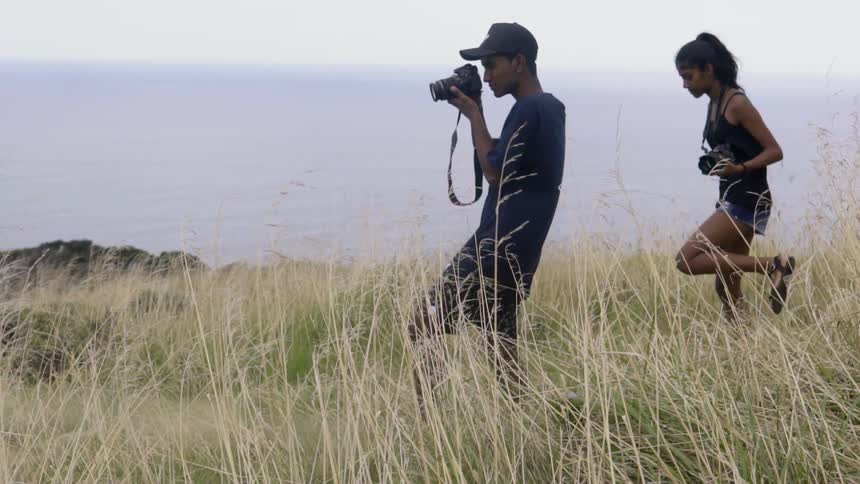 A man and woman carrying cameras walk down a hill on a cloudy day