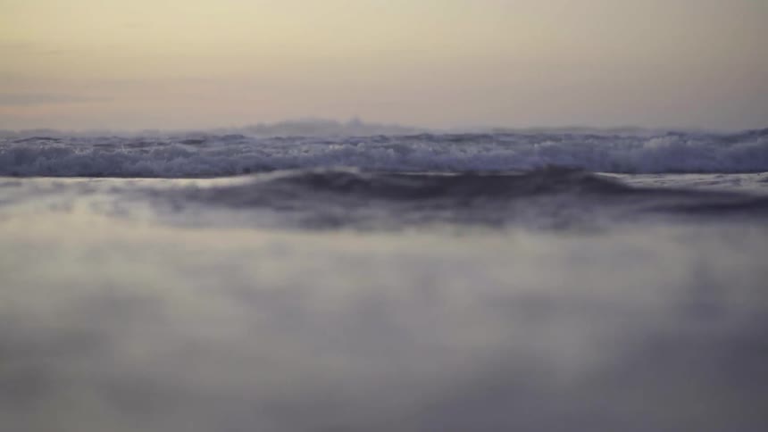 Slow Motion Seascape: Ocean Waves Crashing on Sandy Shore at Dusk.