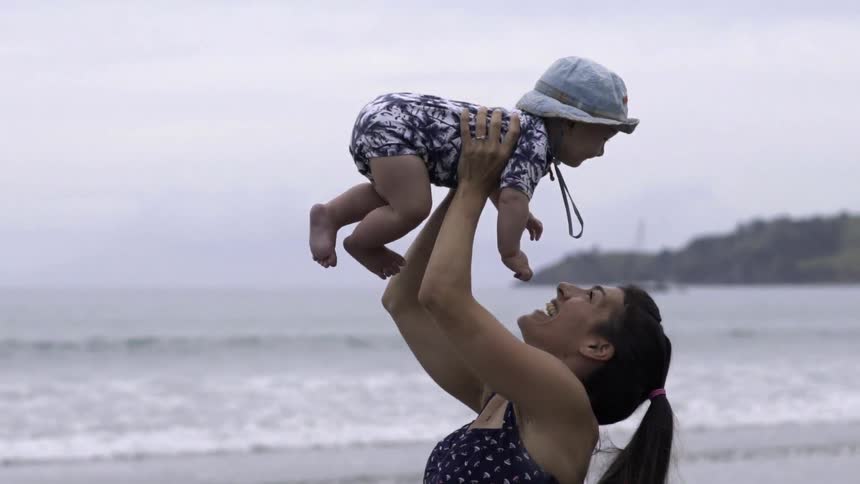 A woman tosses a baby over her head on a cloudy day