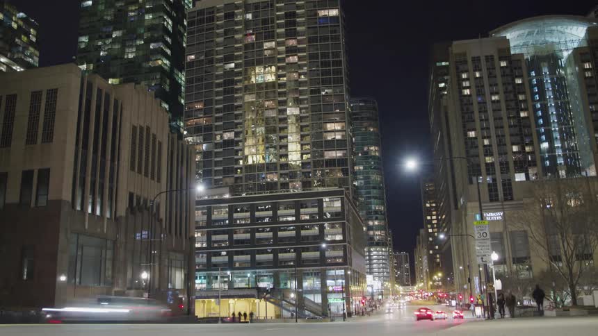 Night view of the illuminated tall buildings with cars going on the road