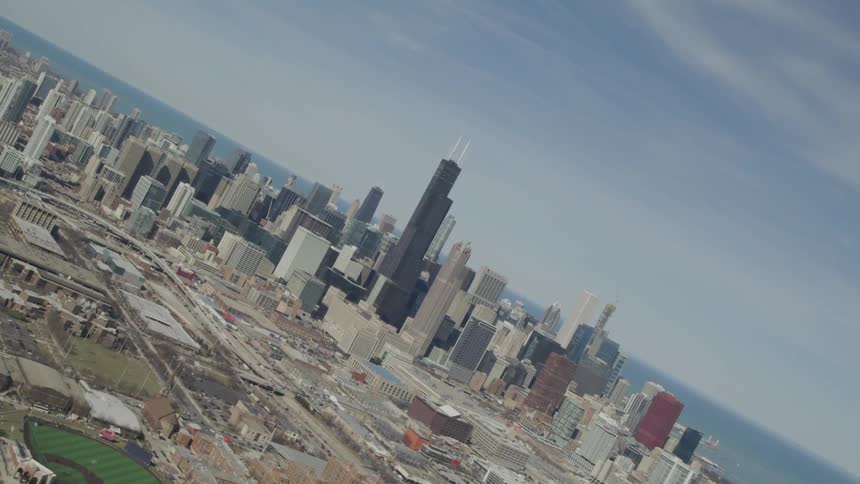 Aerial view of city with tall black skyscraper in the middle and baseball field in front
