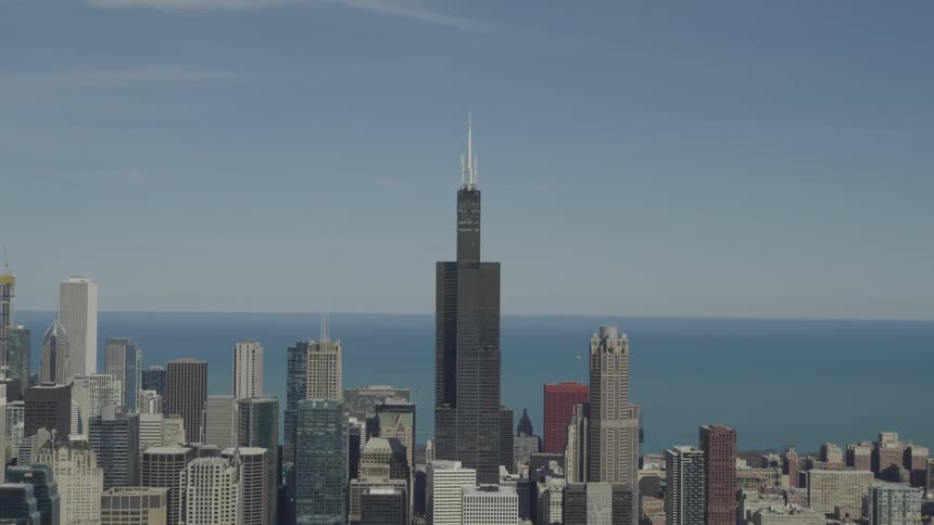 A cityscape with a tall black building in the middle and with the ocean in the background