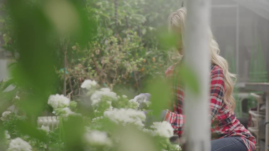 Blonde woman in a checkered shirt works in the garden