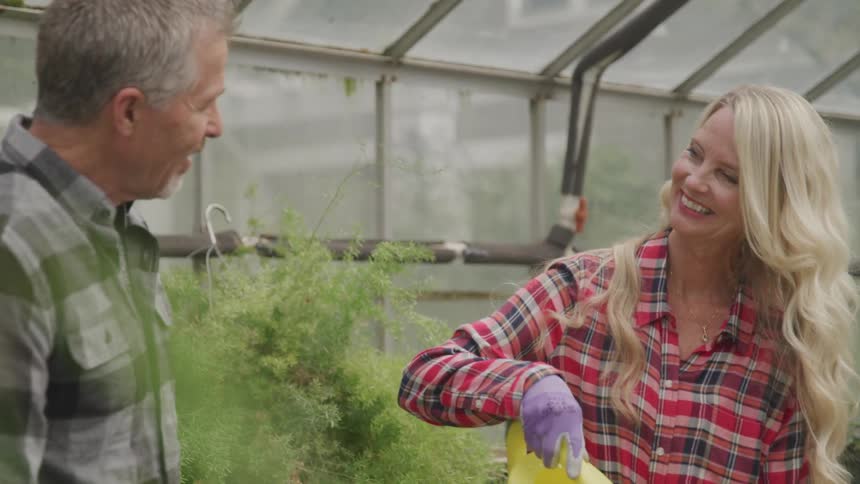 A man and woman in plaid shirts smile while working in a greenhouse