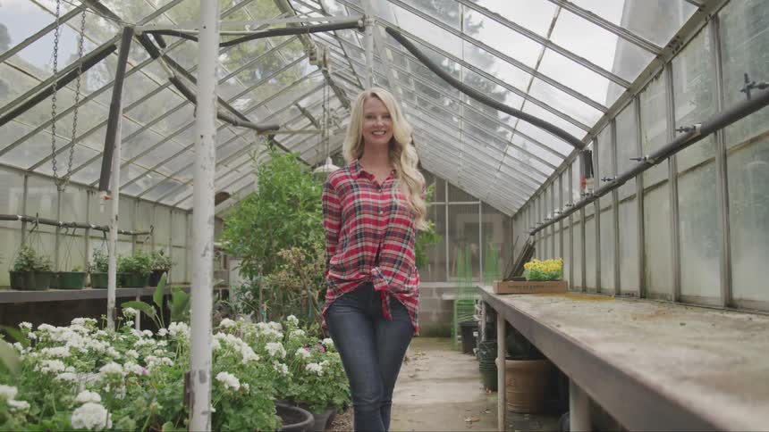 A woman smiles in a large greenhouse