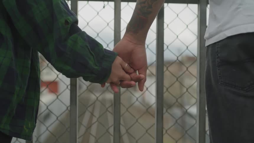 Male and female holding hands in front of a fence