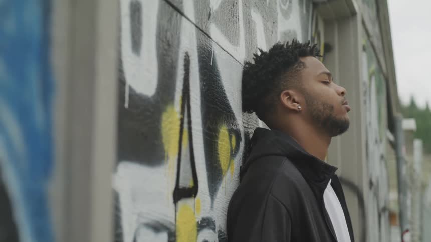 A man outdoors with his head against a wall that has graffiti