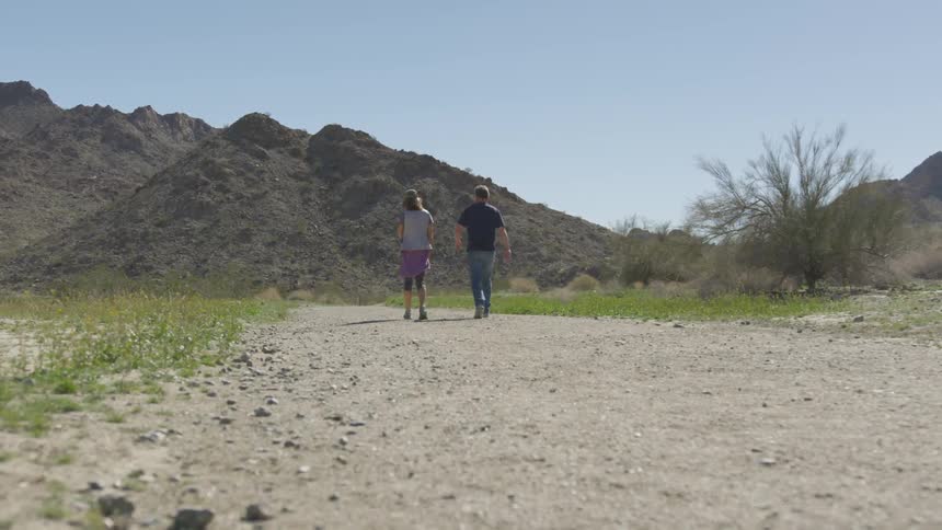Two people walk down a trail together on a sunny day