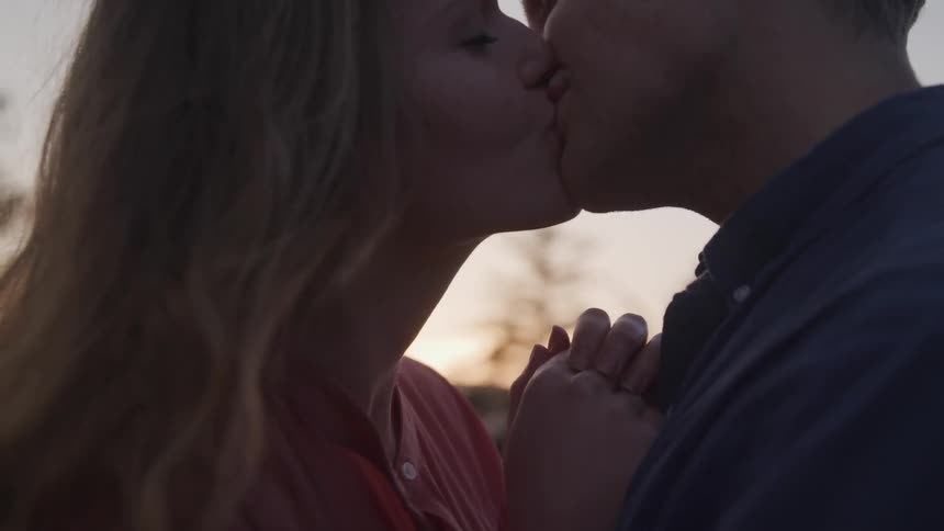 A woman with blonde hair is pressed up against a man as she leans in for a loving kiss and then they both smile