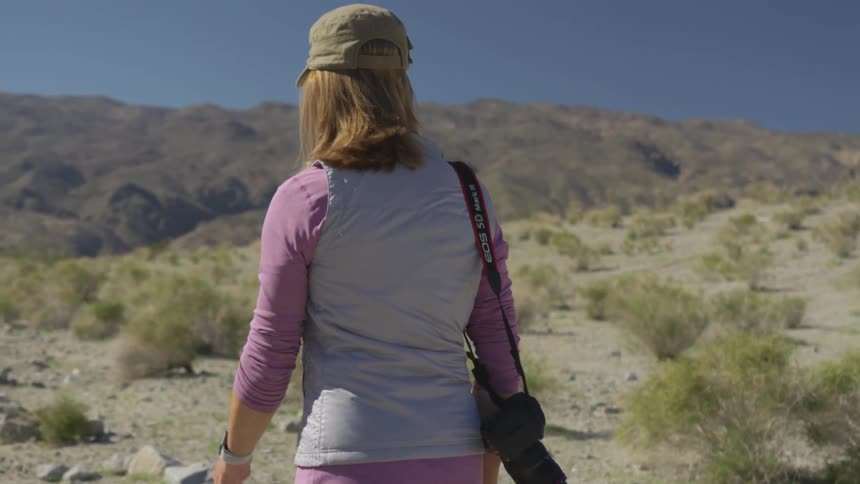 A woman is hiking outdoors while carrying a camera