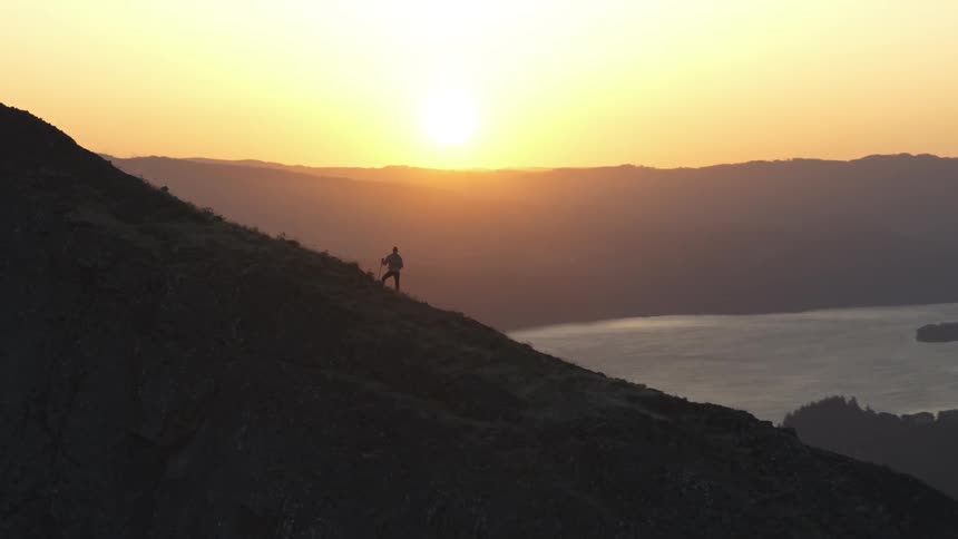 Man climbs mountain while the sun goes down