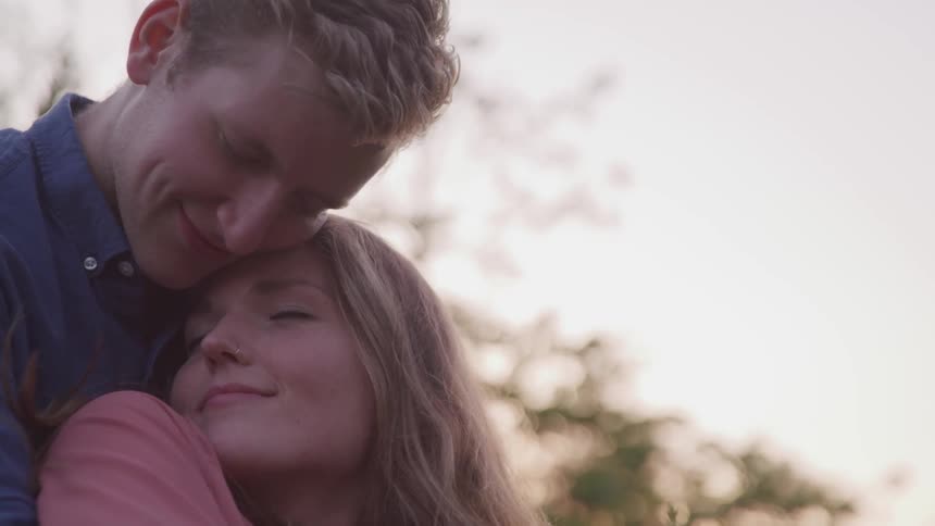 Young couple with eyes closed smiling and cuddling outdoors