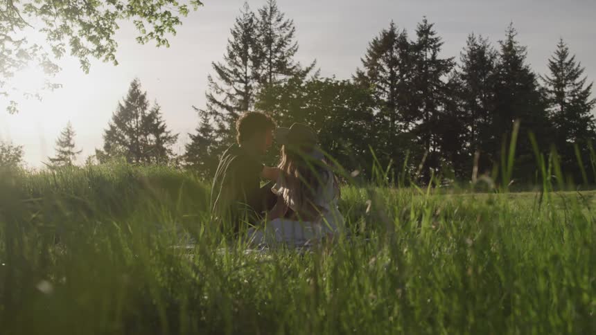 A man and a woman sitting together on a blanket in a field