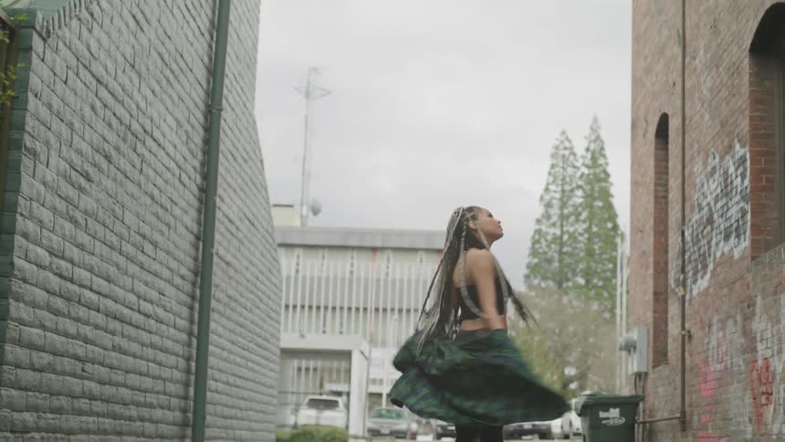 A young black woman dances in a city alley